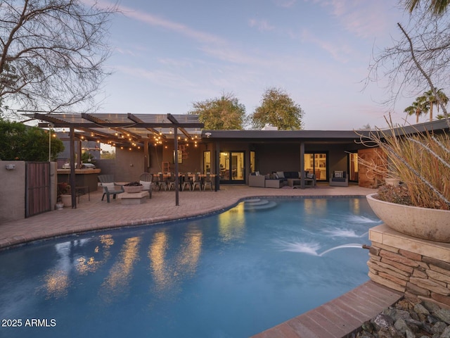 pool at dusk with a patio area, an outdoor pool, and an outdoor living space with a fire pit