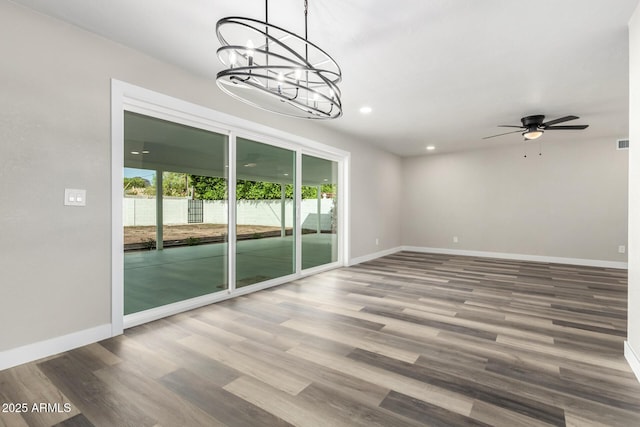 empty room with wood finished floors, visible vents, baseboards, recessed lighting, and ceiling fan with notable chandelier