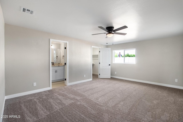 unfurnished bedroom with a spacious closet, visible vents, connected bathroom, baseboards, and light carpet