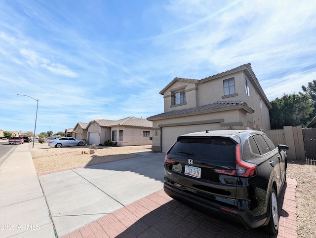 traditional-style home featuring concrete driveway, a tile roof, an attached garage, fence, and stucco siding