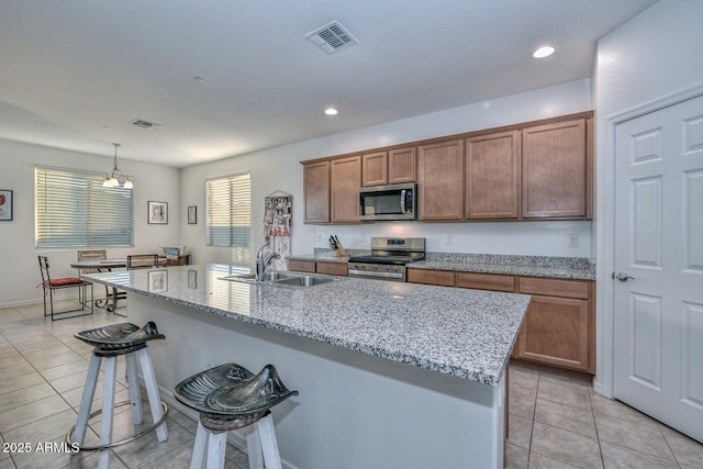 kitchen with sink, a kitchen breakfast bar, an island with sink, pendant lighting, and stainless steel appliances