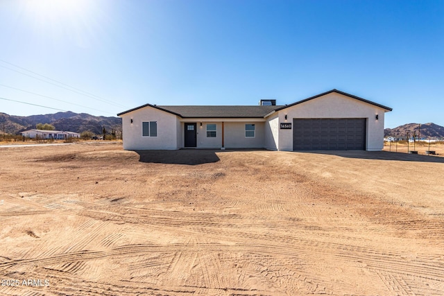 ranch-style home with a garage, a mountain view, driveway, and stucco siding