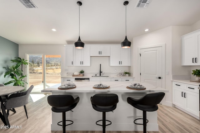 kitchen with light wood-style floors, white cabinetry, visible vents, and a sink