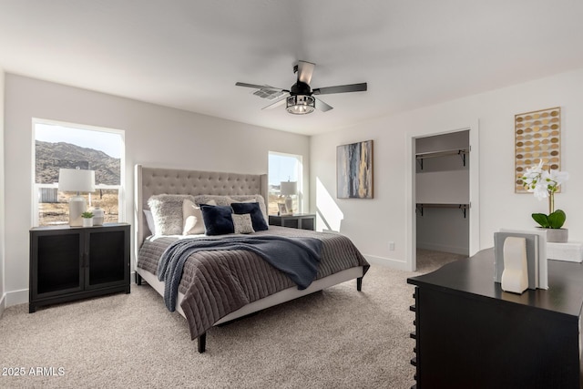 bedroom with light carpet, visible vents, baseboards, a ceiling fan, and a walk in closet