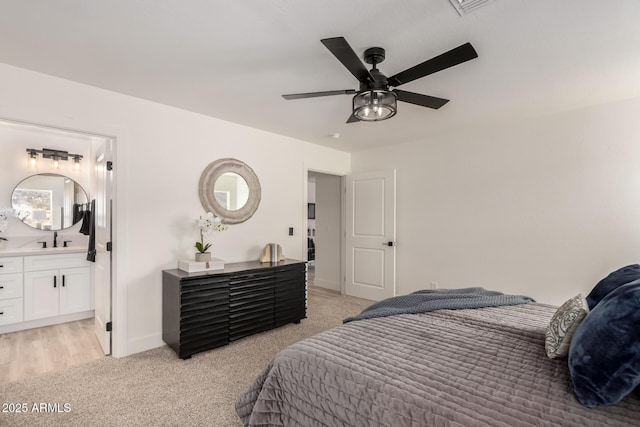 bedroom with ensuite bathroom, light carpet, a sink, a ceiling fan, and baseboards