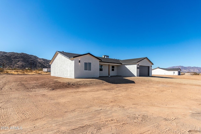 view of front facade featuring an attached garage, dirt driveway, a mountain view, and stucco siding