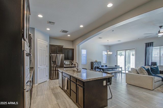 kitchen featuring pendant lighting, a center island with sink, sink, stainless steel appliances, and light stone counters