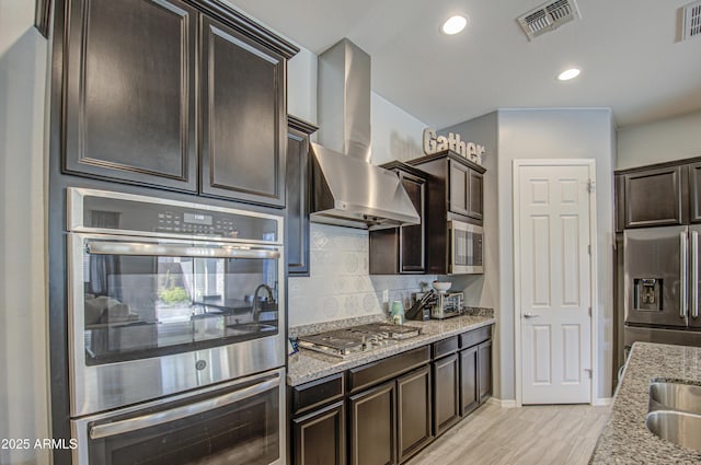 kitchen featuring light hardwood / wood-style floors, dark brown cabinetry, appliances with stainless steel finishes, ventilation hood, and light stone counters