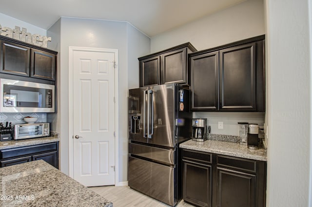 kitchen with light wood-type flooring, stainless steel appliances, dark brown cabinets, and light stone counters