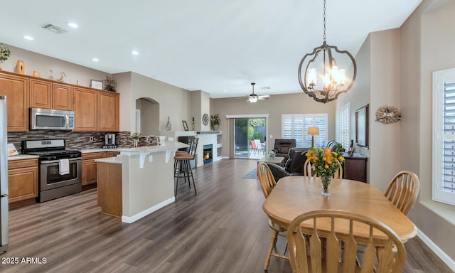 kitchen with stainless steel appliances, backsplash, kitchen peninsula, a kitchen bar, and ceiling fan with notable chandelier