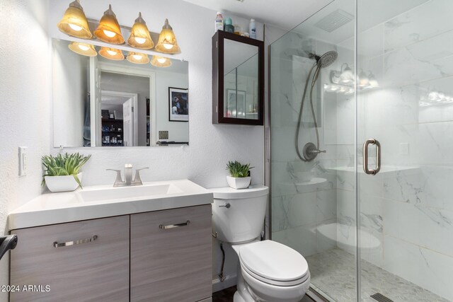 bathroom featuring a shower with door, vanity, and toilet