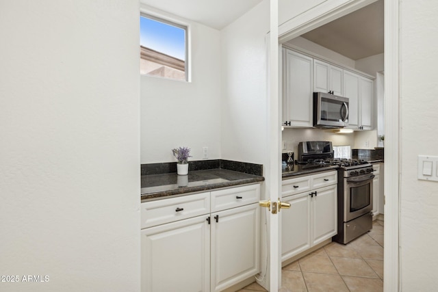 kitchen with dark stone countertops, stainless steel appliances, light tile patterned floors, and white cabinets