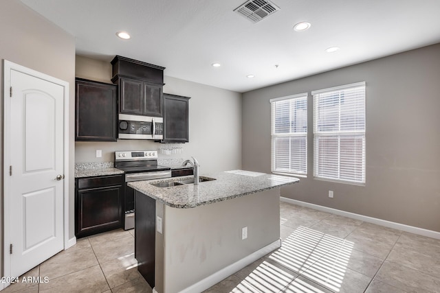 kitchen with a center island with sink, sink, light stone countertops, appliances with stainless steel finishes, and light tile patterned flooring