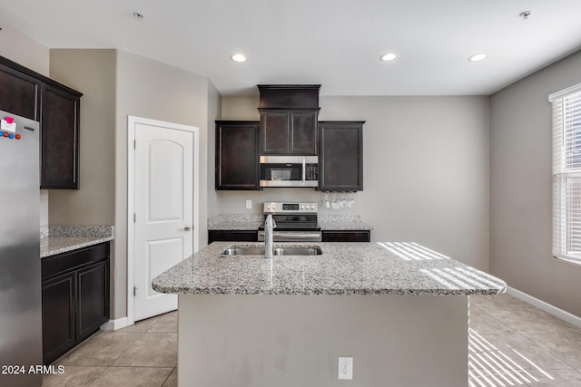 kitchen with dark brown cabinets, light tile patterned floors, stainless steel appliances, and a kitchen island with sink