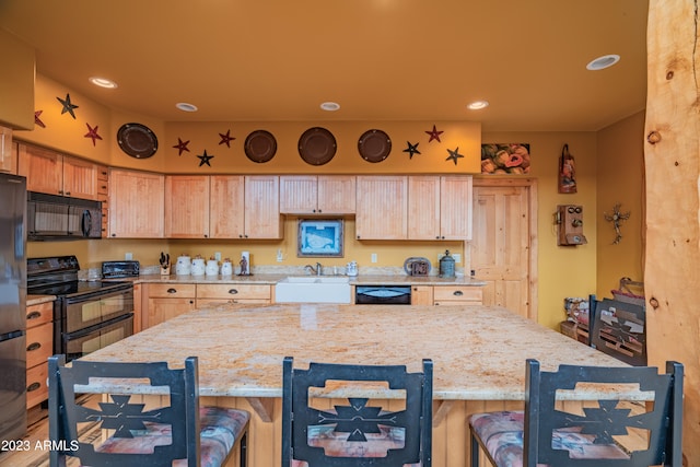 kitchen featuring a breakfast bar area, a kitchen island, sink, and black appliances