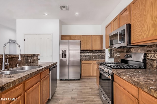 kitchen with dark countertops, a sink, stainless steel appliances, decorative backsplash, and visible vents