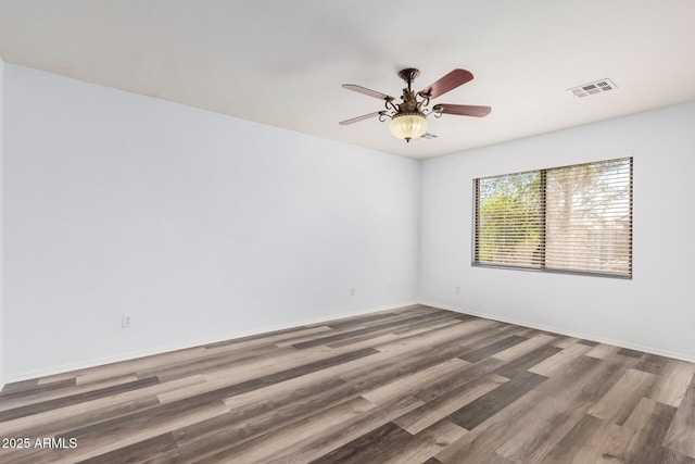 empty room with baseboards, a ceiling fan, wood finished floors, and visible vents