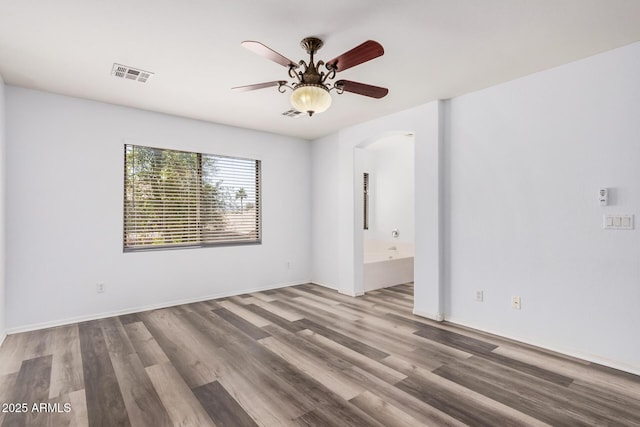 spare room with arched walkways, a ceiling fan, wood finished floors, and visible vents