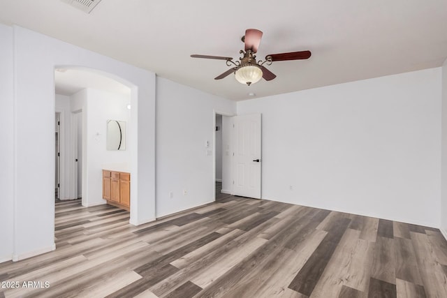 unfurnished bedroom featuring visible vents, ceiling fan, arched walkways, light wood-style flooring, and ensuite bath