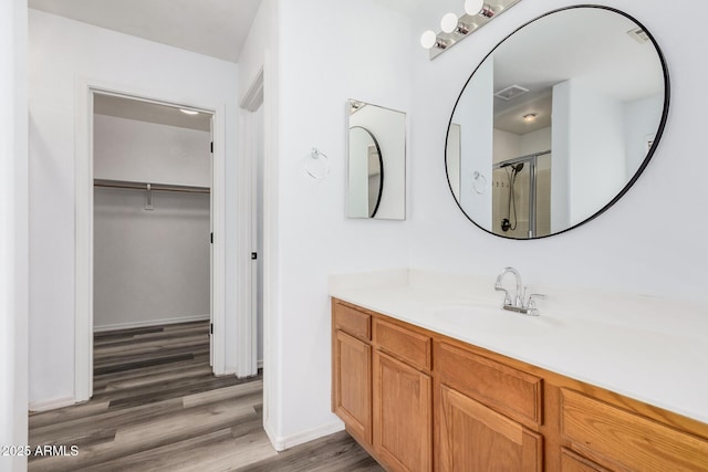 bathroom featuring visible vents, vanity, wood finished floors, a walk in closet, and a shower stall