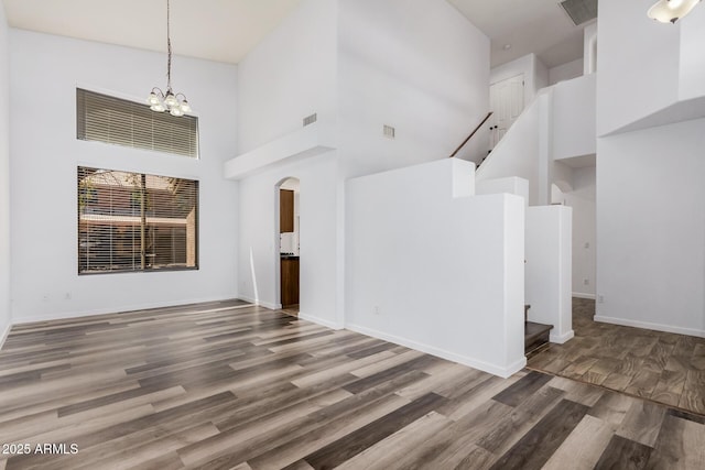 unfurnished living room featuring wood finished floors, a high ceiling, visible vents, and stairway