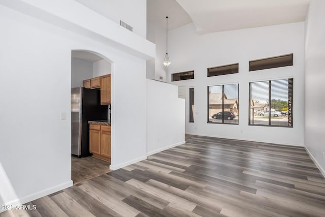 unfurnished living room featuring visible vents, arched walkways, baseboards, high vaulted ceiling, and dark wood-style floors