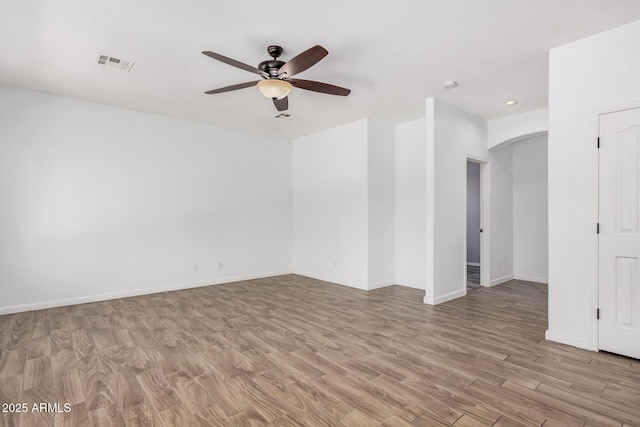 empty room featuring visible vents, wood finished floors, baseboards, arched walkways, and a ceiling fan