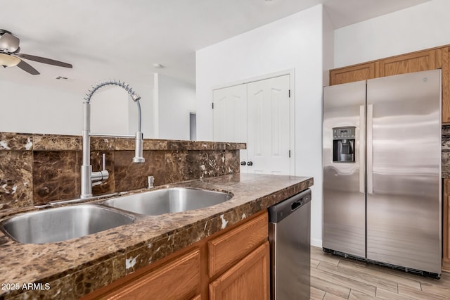 kitchen with ceiling fan, dark countertops, appliances with stainless steel finishes, a sink, and light wood-style flooring