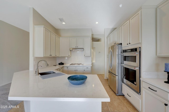 kitchen with light tile patterned floors, stainless steel appliances, a sink, a peninsula, and under cabinet range hood