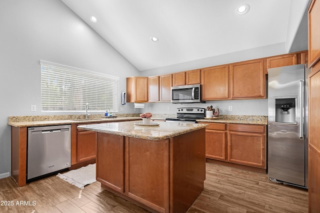 kitchen featuring appliances with stainless steel finishes, light stone counters, wood finished floors, and a center island