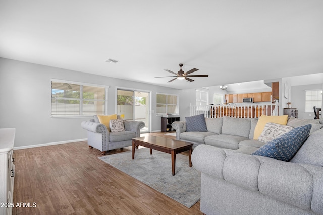 living area featuring a ceiling fan, baseboards, visible vents, and wood finished floors