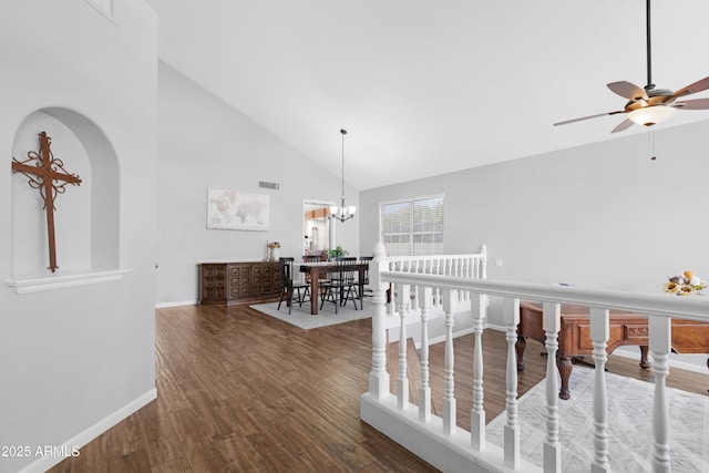 hallway with high vaulted ceiling, a notable chandelier, wood finished floors, visible vents, and baseboards