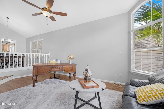 living room featuring ceiling fan with notable chandelier, lofted ceiling, baseboards, and wood finished floors