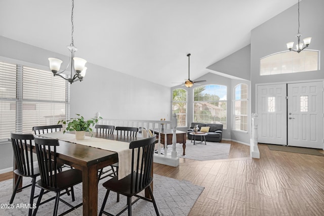 dining space with high vaulted ceiling, ceiling fan with notable chandelier, baseboards, and wood finished floors