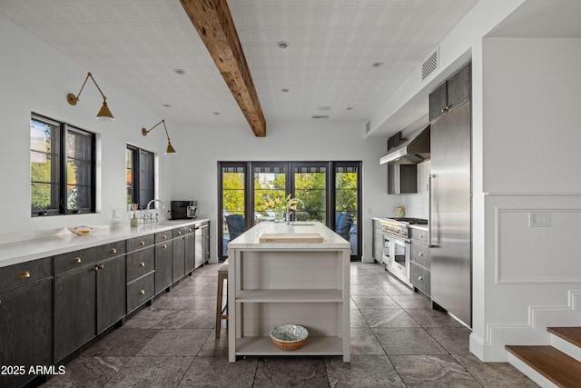 kitchen featuring sink, a kitchen breakfast bar, beamed ceiling, a kitchen island with sink, and wall chimney range hood