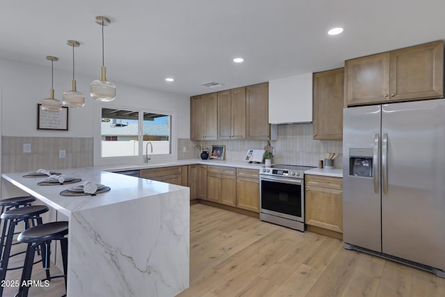 kitchen featuring stainless steel appliances, a peninsula, a kitchen breakfast bar, wall chimney exhaust hood, and decorative light fixtures