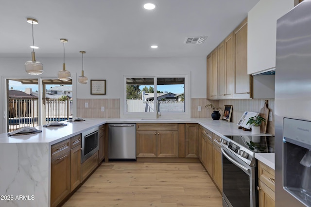 kitchen featuring decorative light fixtures, visible vents, appliances with stainless steel finishes, a sink, and a peninsula