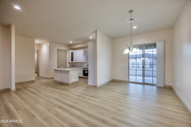 unfurnished living room with a sink, baseboards, an inviting chandelier, and light wood-style flooring
