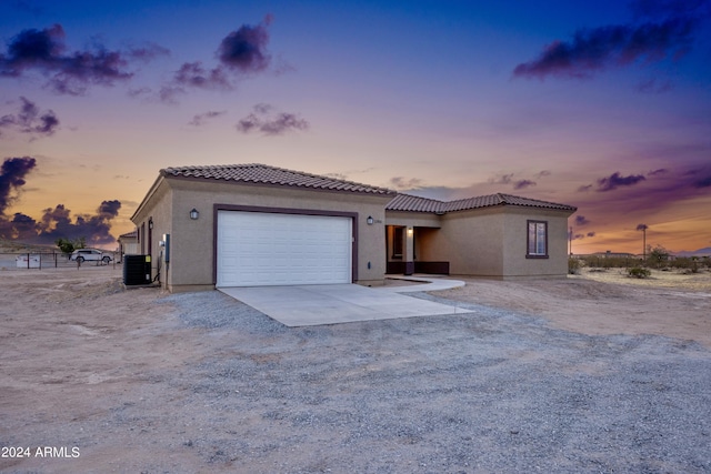 view of front facade with central AC, stucco siding, an attached garage, driveway, and a tile roof