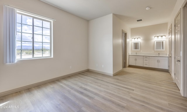 unfurnished bedroom with light wood-type flooring, baseboards, and ensuite bath