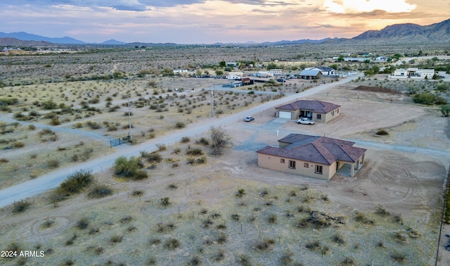 aerial view at dusk featuring a mountain view, view of desert, and a rural view