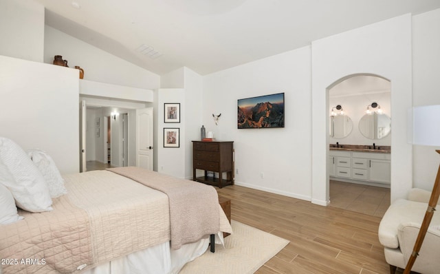 bedroom featuring lofted ceiling, sink, ensuite bath, and light hardwood / wood-style flooring