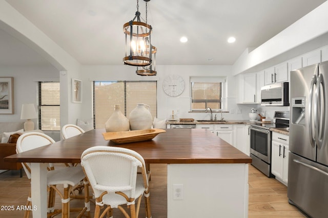 kitchen with wood counters, a center island, appliances with stainless steel finishes, pendant lighting, and white cabinets