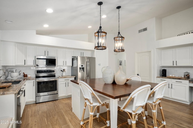 kitchen featuring sink, stainless steel appliances, light hardwood / wood-style floors, white cabinets, and decorative light fixtures