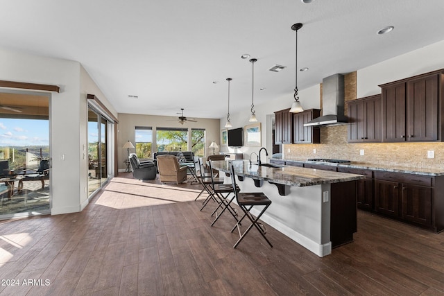 kitchen with a center island with sink, dark hardwood / wood-style flooring, wall chimney range hood, and stone counters