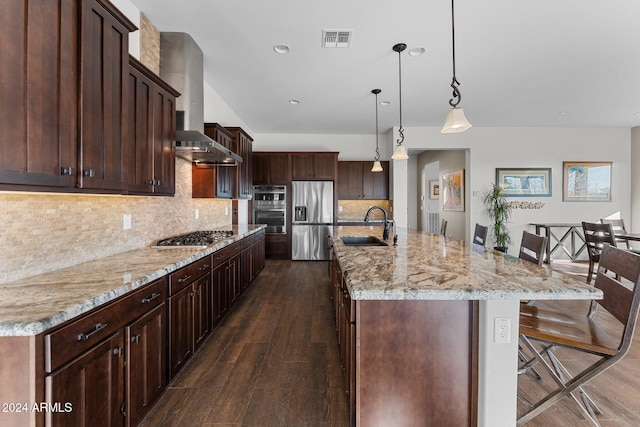 kitchen featuring wall chimney exhaust hood, dark wood-type flooring, stainless steel appliances, pendant lighting, and a spacious island