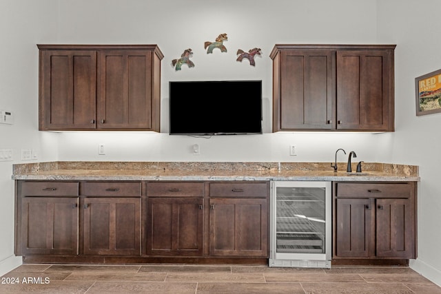 bar with dark brown cabinetry, light hardwood / wood-style floors, light stone counters, and beverage cooler