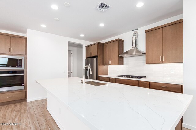 kitchen with light hardwood / wood-style flooring, appliances with stainless steel finishes, an island with sink, sink, and decorative backsplash