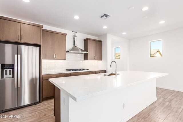 kitchen with an island with sink, sink, light wood-type flooring, and stainless steel refrigerator with ice dispenser