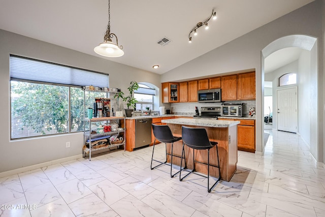 kitchen with tasteful backsplash, appliances with stainless steel finishes, a kitchen breakfast bar, a kitchen island, and pendant lighting